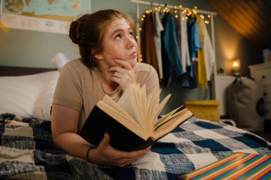 Genç, düşünceli, düşünceli bir kız. Kitabı açtı. Evdeki rahat bir odada yatarken yan yana baktı ve çenesine dokundu.