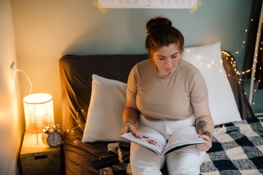 Genç, güzel, sakin bir kız ve dergi evdeki rahat odada, yatağında oturuyor.