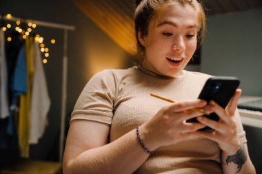 Evde rahat bir odada otururken, elinde telefonla ona bakan güzel, hevesli bir kızın portresi.