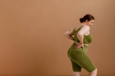 Beyaz kadın gülümseyip poz verirken bej arka planda tek başına duruyor.