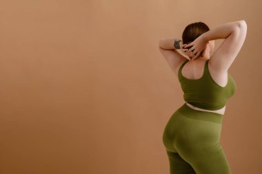 Beyaz kadın gülümseyip poz verirken bej arka planda tek başına duruyor.