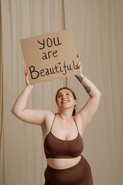 Beyaz kadın gülümseyip işaret ederken bej arka planda izole edilmiş bir pankart gösteriyor.