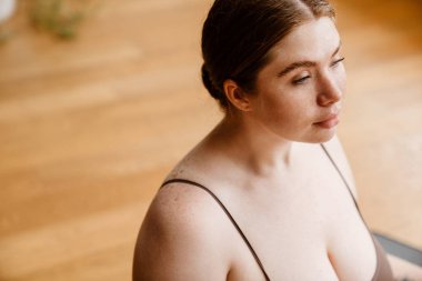 Evde yoga yaparken mindere oturan kızıl saçlı genç kadın.