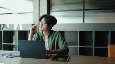 Gözlüklü esmer Asyalı bir adamın laptopla çalışıp çalışma odasında yazı yazması.