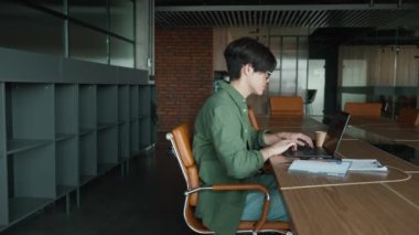 Ofiste dizüstü bilgisayarda yazan, gözlüklü, kendine güvenen Asyalı adam.