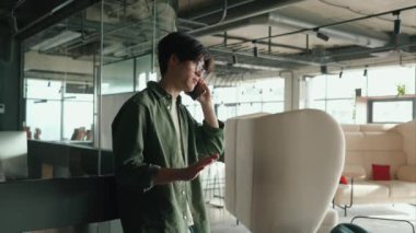 Brunet Asyalı gözlüklü bir adam çalışma odasında akıllı telefondan konuşuyor.