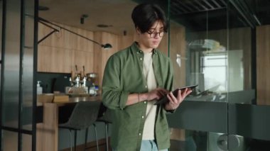 Gözlüklü, kendine güvenen esmer Asyalı bir adam çalışma odasında tablet üzerinde çalışıyor.