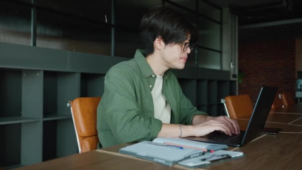 Snygg Asiatisk Man Glasögon Arbetar Bärbar Dator Vid Ett Skrivbord — Stockvideo