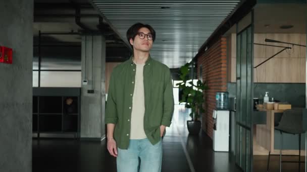 美しいブルネットのアジア人男性が眼鏡をかけて共同作業室を歩いている — ストック動画