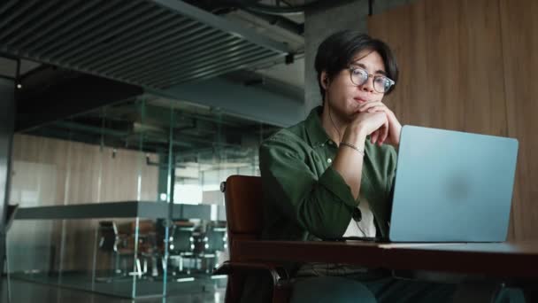 オフィスのヘッドフォンでノートパソコンで何かを見ているアジアの男性 — ストック動画