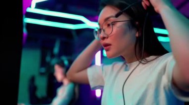 Positive Asian woman gamer puts on headphones to play RPG video game on a championship. Stylish Neon Cyber Games