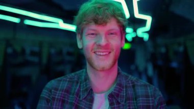 Smiling ginger man gamer posing at the camera after playing RPG video game on a championship. Stylish Neon Cyber Games