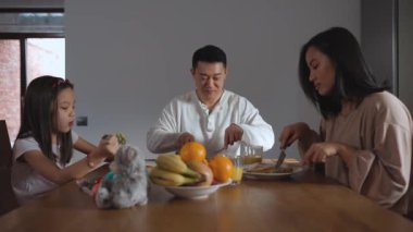 Gülümseyen Asyalı aile evdeki mutfakta kahvaltı yapıyor.