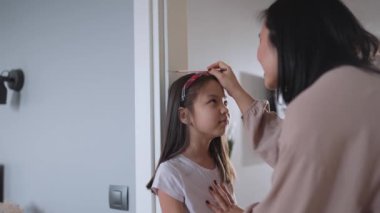 Tatlı Asyalı anne kızının boyunu evde ölçüyor.
