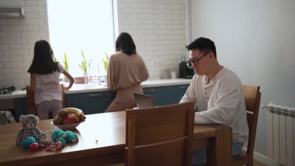 Geconcentreerde Aziatische Vader Werkt Laptop Terwijl Mam Dochter Maken Ontbijt — Stockvideo