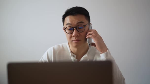 Morena Sorridente Homem Asiático Vestindo Óculos Trabalhando Laptop Falando Telefone — Vídeo de Stock