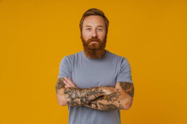 Sakallı mutlu adam sarı arka planda tek başına dikilirken kameraya poz veriyor.