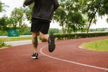 Siyah spor takım elbiseli bir yetişkinin baldırında açık havada koşan dövmeli portresi.