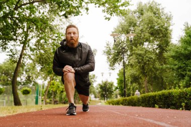 Kızıl sakallı sporcu dışarıda parkta çalışırken egzersiz yapıyor.