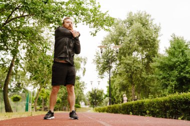 Kızıl sakallı sporcu dışarıda parkta çalışırken egzersiz yapıyor.