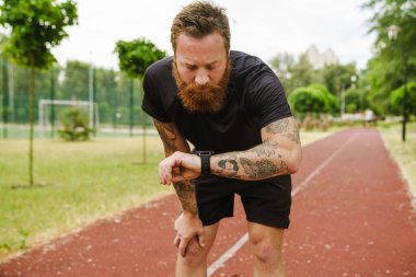 Zencefilli sakallı sporcu dışarıda parkta çalışırken akıllı seğirme kullanıyor.