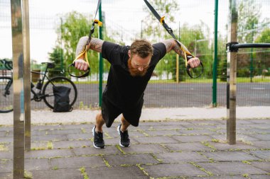 Kızıl sakallı sporcu dışarıda oyun oynarken egzersiz yapıyor.