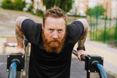 Kızıl sakallı sporcu dışarıda oyun alanında egzersiz yapıyor.