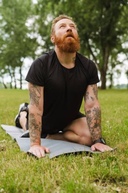 Kızıl sakallı adam parkta yoga yaparken egzersiz yapıyor.