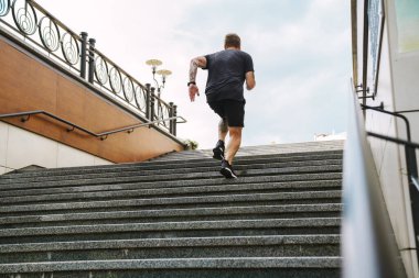 Kızıl sakallı sporcu dışarıda çalışırken merdivenlerde koşuyor.