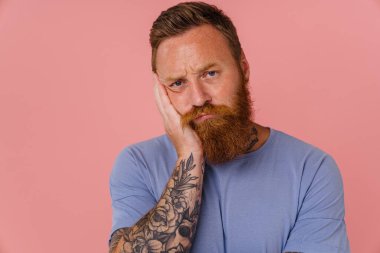 Kızıl saçlı, sakallı, kafası karışmış ve pembe arka planda izole edilmiş kameraya bakan adam.