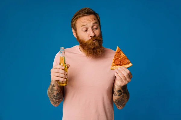 Portrait of confused white man choosing between pizza and beer apple isolated over blue background