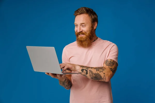 Brodaty Szczęśliwy Człowiek Trzymając Laptopa Stojąc Odizolowany Nad Niebieskim Tle — Zdjęcie stockowe