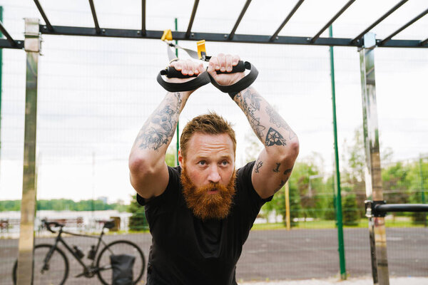 Ginger bearded sportsman doing exercise while working out on playground outdoors