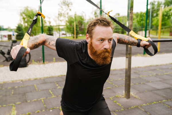 Ginger bearded sportsman doing exercise while working out on playground outdoors