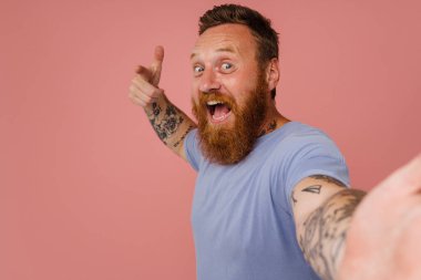 Kızıl heyecanlı bir adam pembe arka planda izole edilmiş selfie ve jest çekiyor.