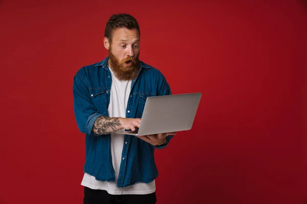 Імбирний Шокований Чоловік Джинсовій Сорочці Ноутбуком Ізольований Червоному Тлі — стокове фото