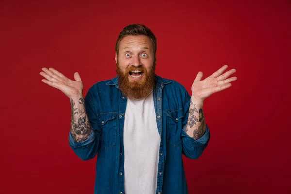 Ginger Shocked Man Tattoo Expressing Surprise Camera Isolated Red Background — Stock Photo, Image