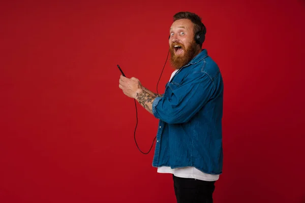 Kızıl Saçlı Kulaklıklı Müzik Dinleyen Kırmızı Arka Planda Izole Edilmiş — Stok fotoğraf