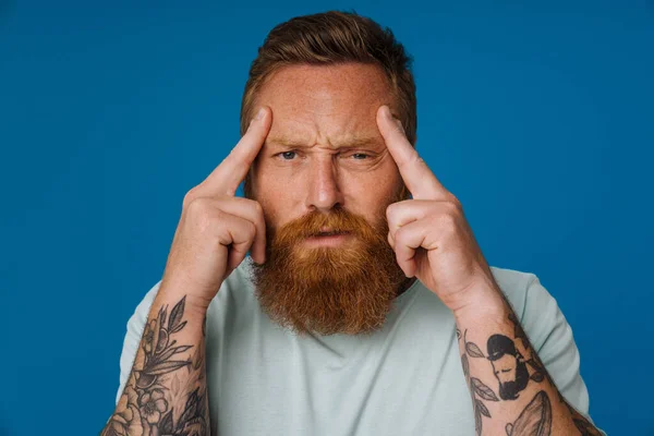 Ginger puzzled man with headache rubbing his temples isolated over blue background