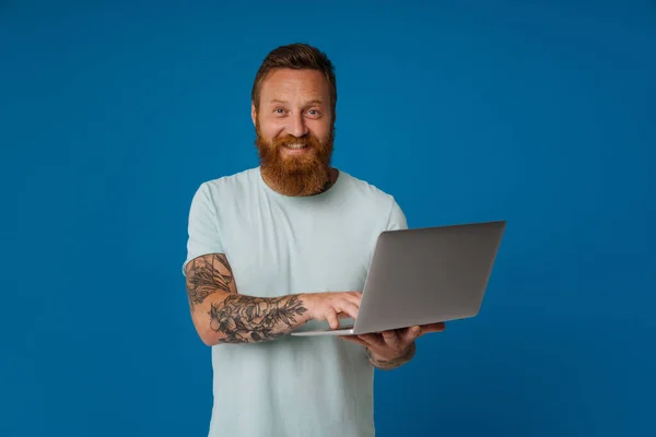 Rudy Podekscytowany Mężczyzna Tatuażem Uśmiecha Się Pracuje Laptopem Izolowane Niebieskim — Zdjęcie stockowe