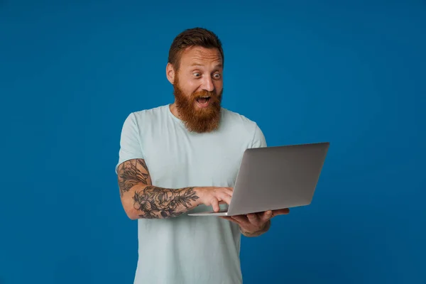 Imbir Podekscytowany Człowiek Tatuażem Krzyczy Pracuje Laptopem Izolowane Niebieskim Tle — Zdjęcie stockowe