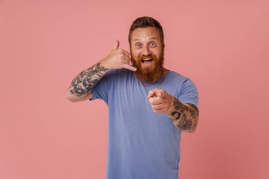 Ginger heyecanlı sakallı, gülümseyen ve pembe arka planda izole edilmiş hareketler yapan adam.