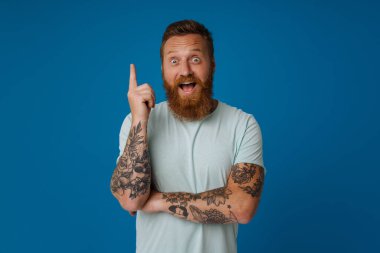 Ginger heyecanlı adam gülümsüyor ve mavi arka planda parmaklarını yukarı kaldırıyor.