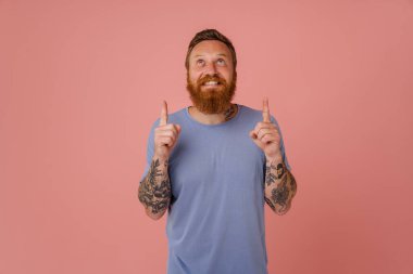 Kızıl beyaz adam gülümsüyor ve pembe arka planda parmaklarını yukarı kaldırıyor.