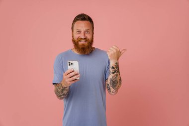 Kizil beyaz adam cep telefonu kullaniyor ve pembe arka plan uzerinde ayrilmis bir parmakla gösteriyor.