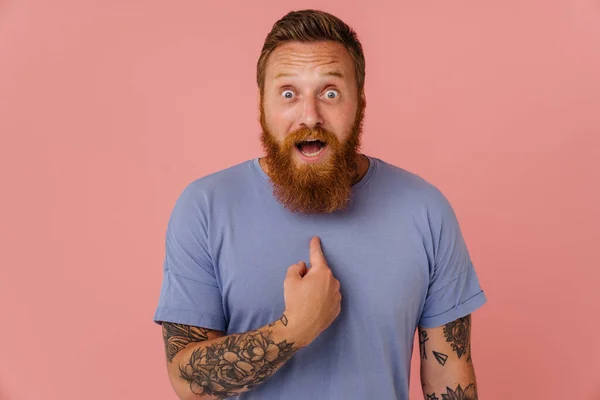 Ginger shocked man screaming and pointing finger at himself isolated over pink background