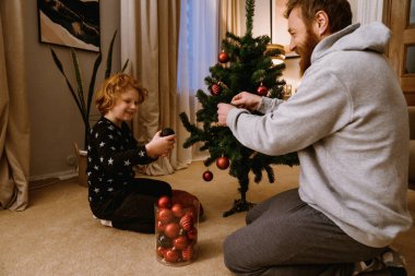 Neşeli baba ve oğul evdeki rahat oturma odasında Noel ağacı süslüyorlar.