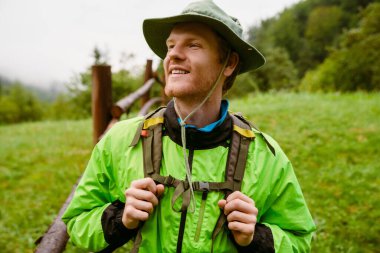 Sırt çantalı genç turist ahşap çitlerin yanında duruyor ve dağlarda yürürken gözlerini kaçırıyor.