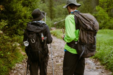 Sırt çantalı ve kırsalda yürüyüş yapan genç turist çiftin arka görüntüsü.