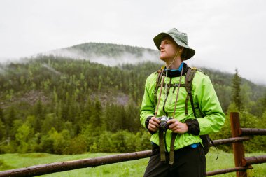 Ahşap çitlerin yanında duran ve dağlarda yürüyüş yaparken gözlerini kaçıran genç turist.